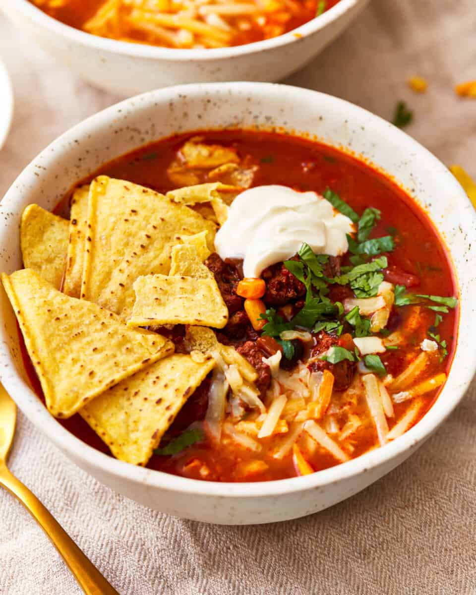 Two bowls of mexican soup with tortillas and sour cream.
