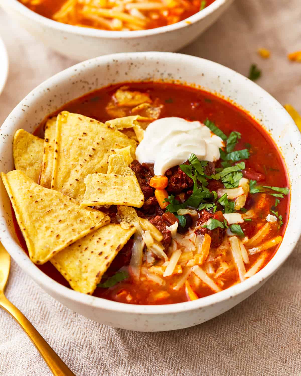 A bowl of tortilla soup with ground beef, cheese, tortilla chips, and sour cream.