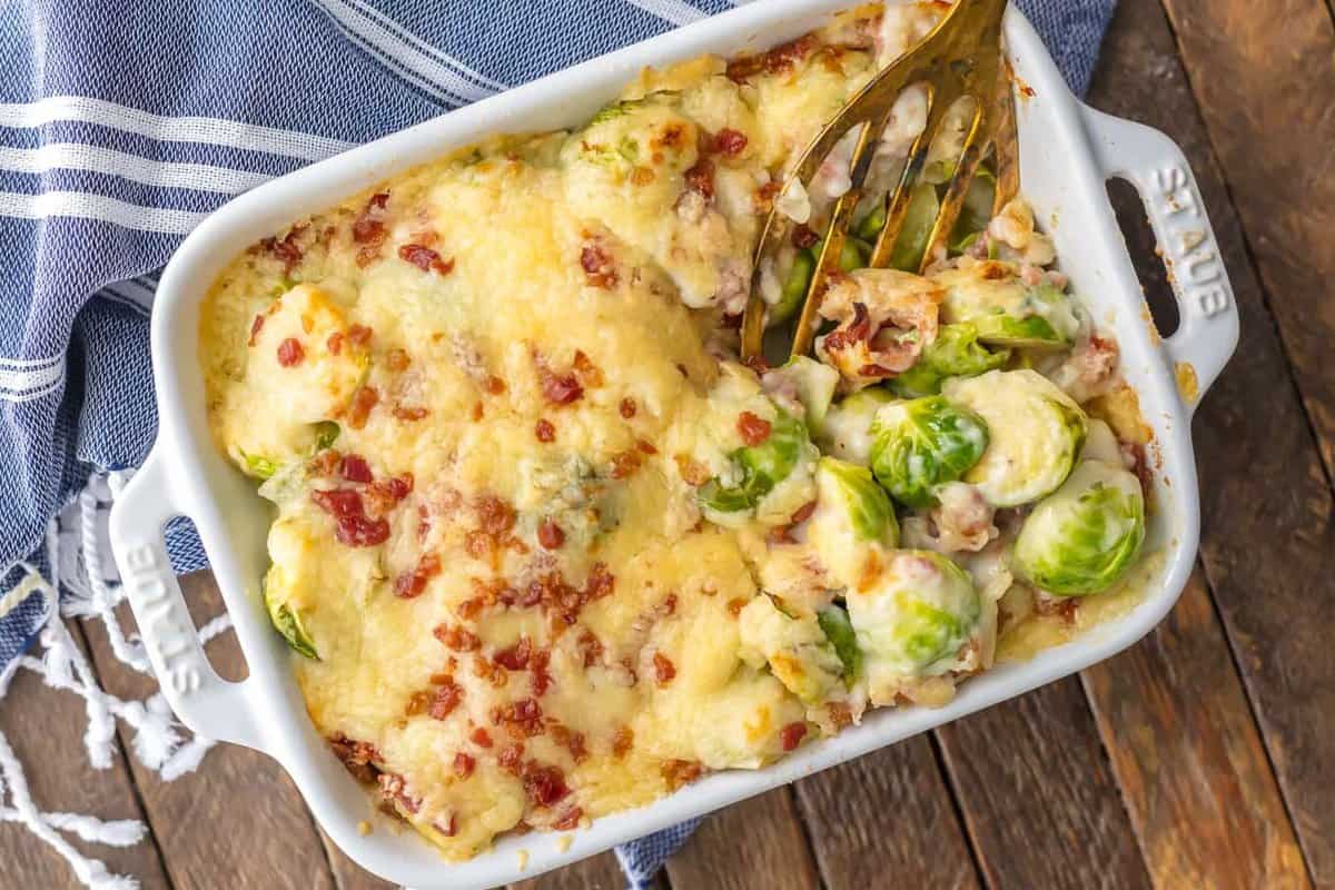 Bacon Brussels Sprouts Gratin in a white baking dish, sitting on a blue and white striped dish towel
