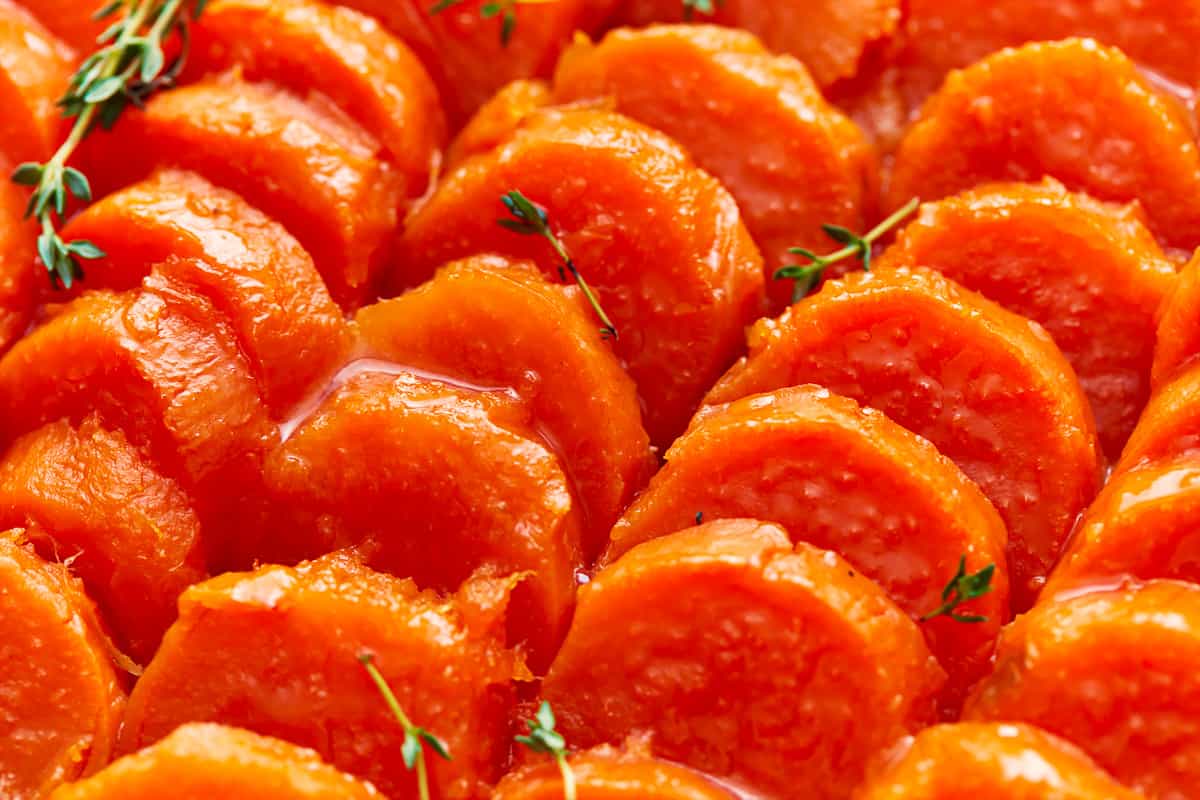 A close up of candied sweet potatoes with thyme sprigs.