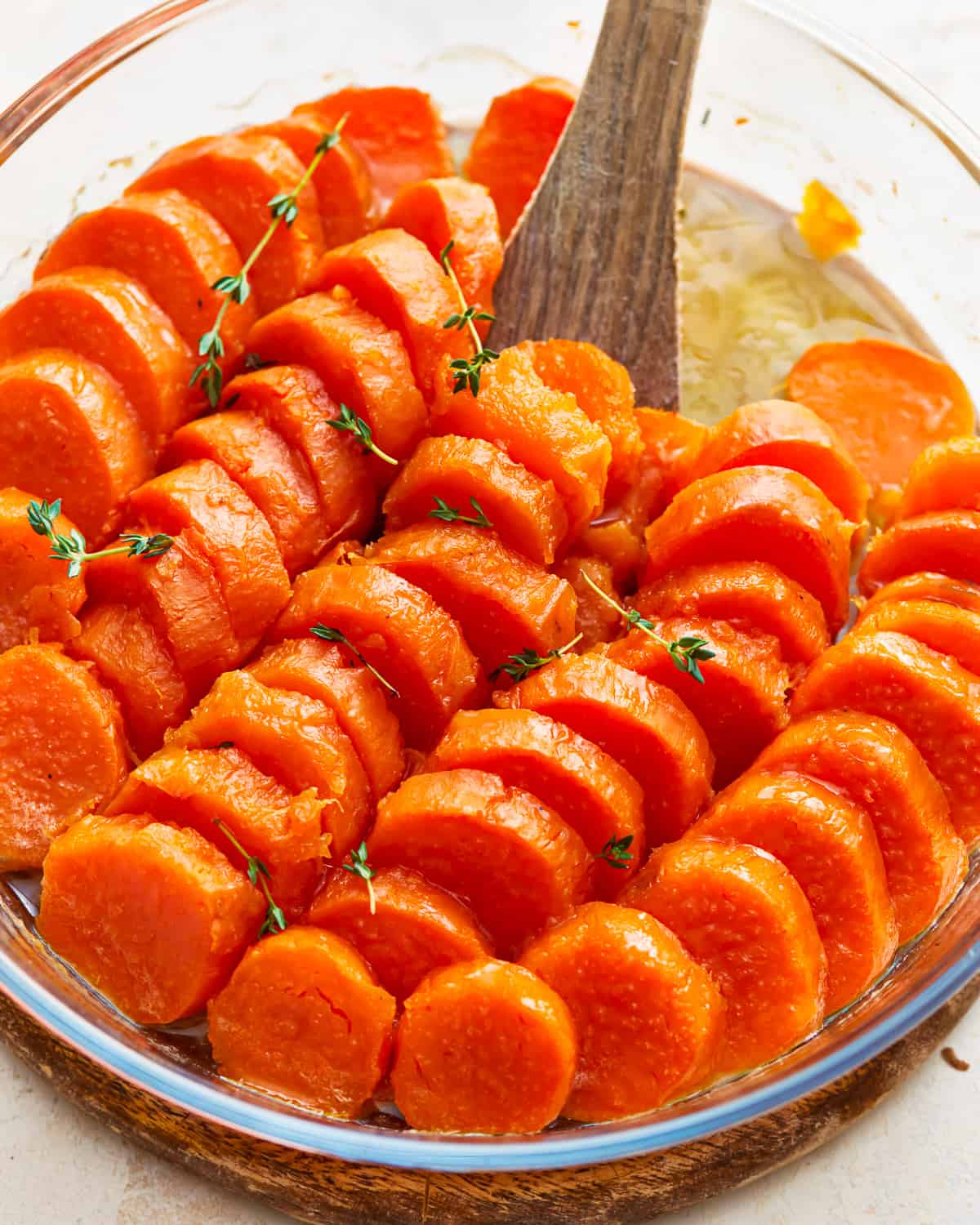 Candied sweet potatoes in a glass baking dish with a wooden spoon.