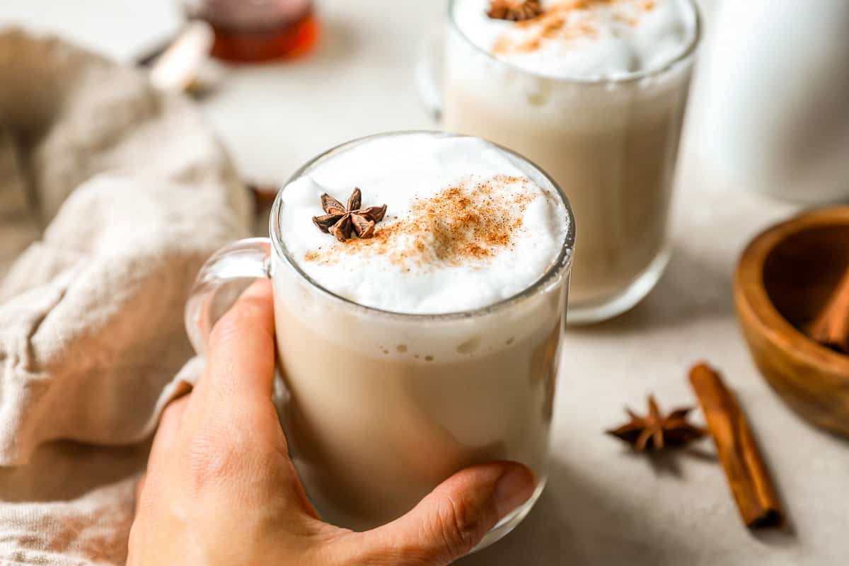 A person holding a mug of chai tea latte with cinnamon and anise.