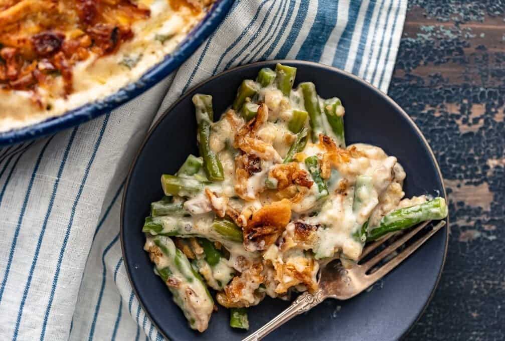 Classic Green Bean Casserole is one of those Thanksgiving recipes that you don't need to reinvent. It's absolutely perfect just the way it is, with green beans, cream of mushroom, crunchy fried onions, and some other awesome ingredients. This green bean casserole recipe is exactly what you need for you next holiday meal! A serving of creamy green beans on a plate with a fork.