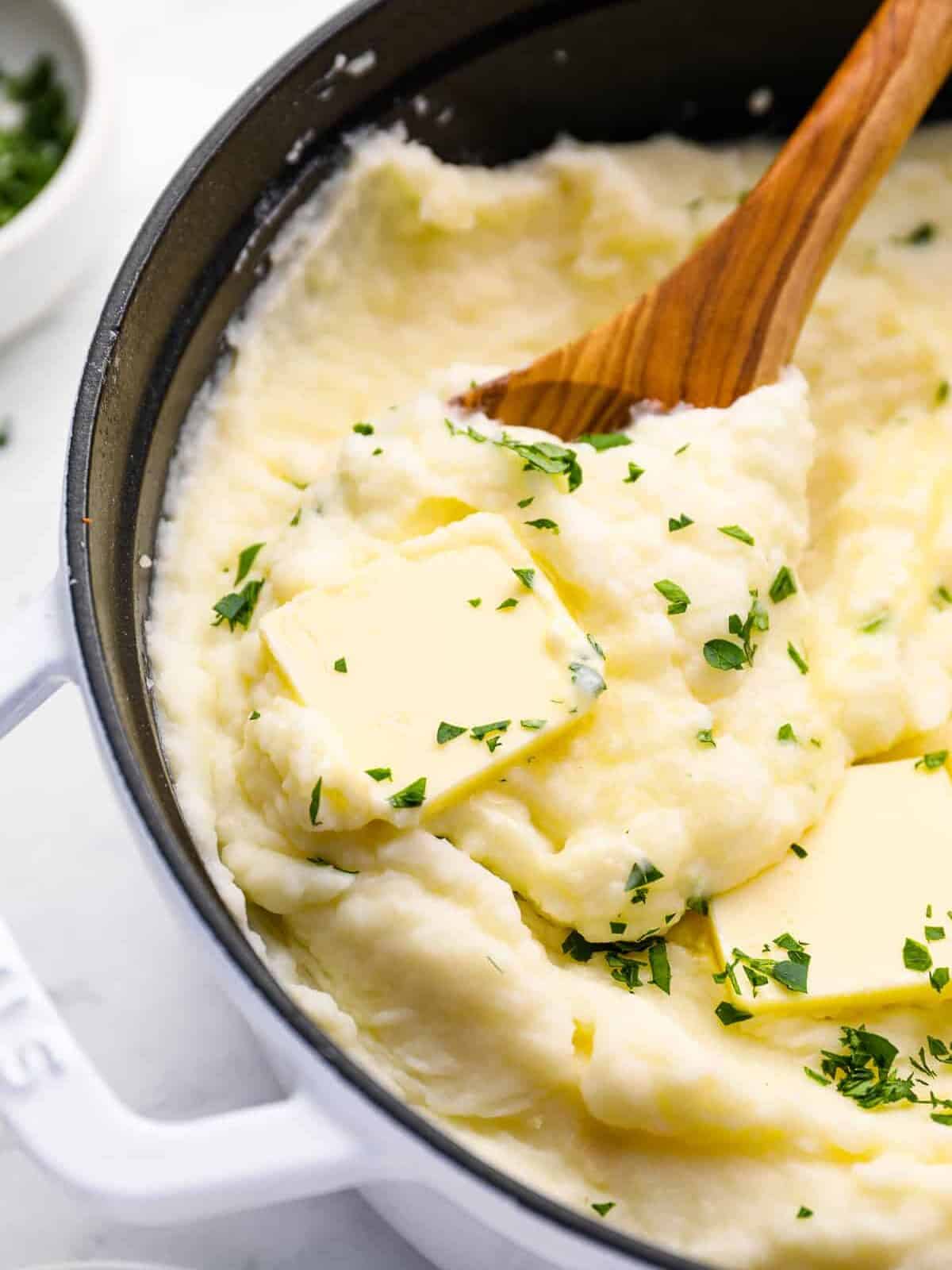 mashed potatoes in a cast iron skillet with a wooden spoon.