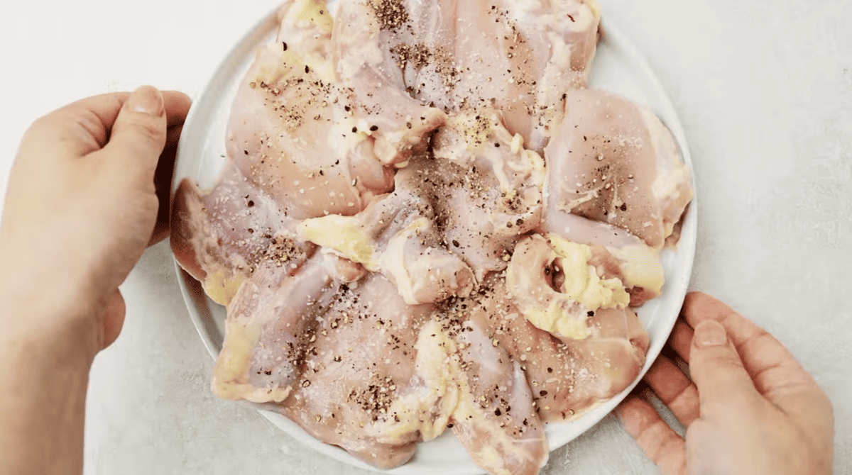 A person holding a plate with succulent chicken breasts topped with dumplings.