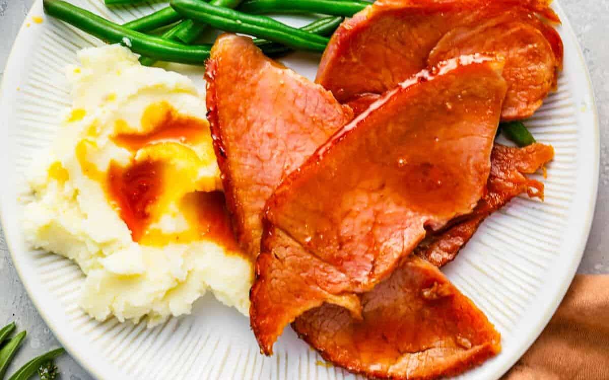 A plate with ham, green beans and mashed potatoes.