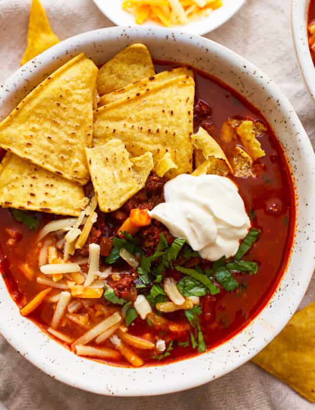 A bowl of beef tortilla soup with tortilla chips and sour cream.