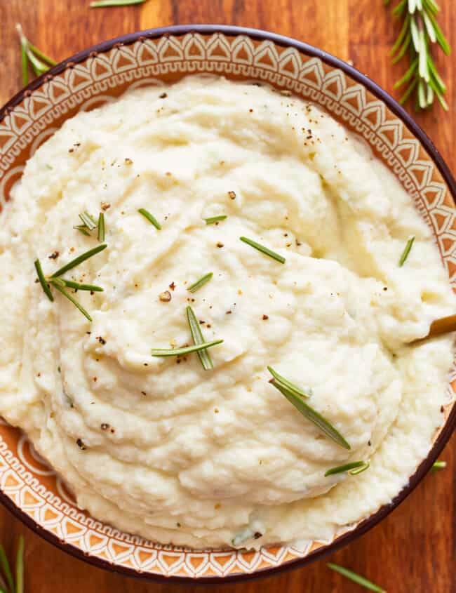 A bowl of mashed cauliflower with rosemary sprigs.