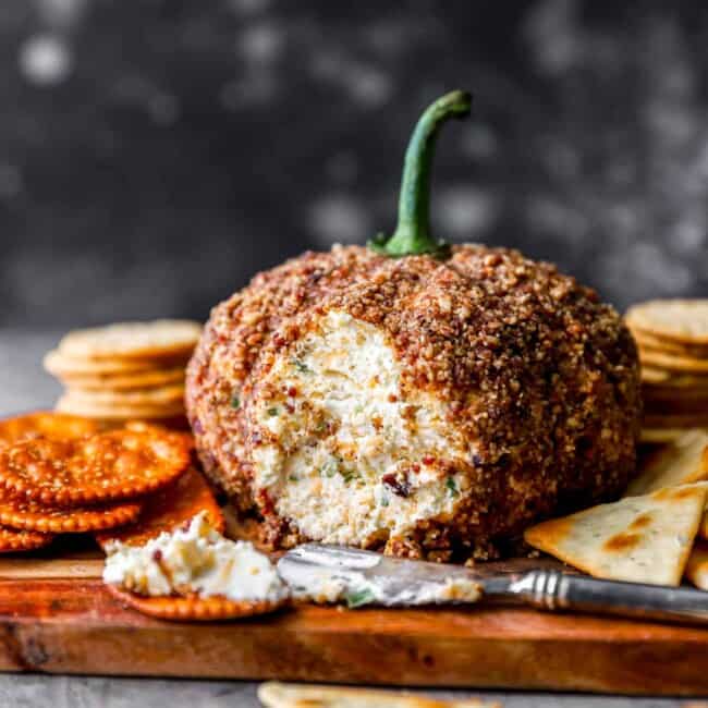 Pumpkin cheese ball on a cutting board with crackers.