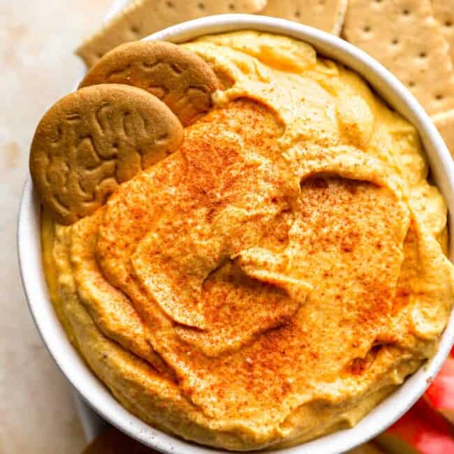 A bowl of pumpkin hummus with crackers and crackers.