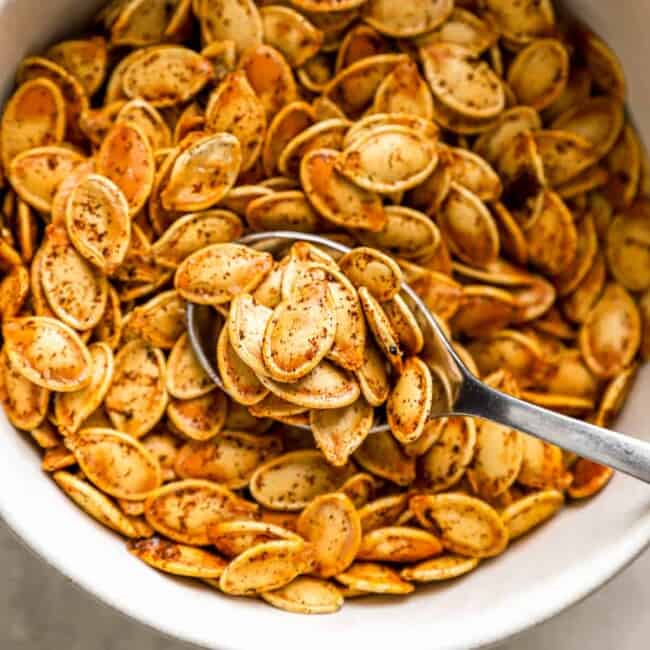 Pumpkin seeds in a bowl with a spoon.