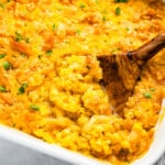 Cheesy corn casserole in a white dish with a wooden spoon.