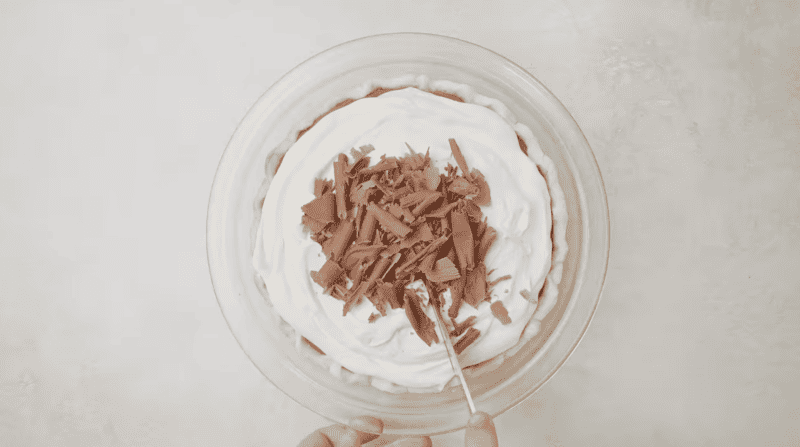 overhead view of cutting a french silk pie with whipped cream and chocolate shavings in a glass pie dish.