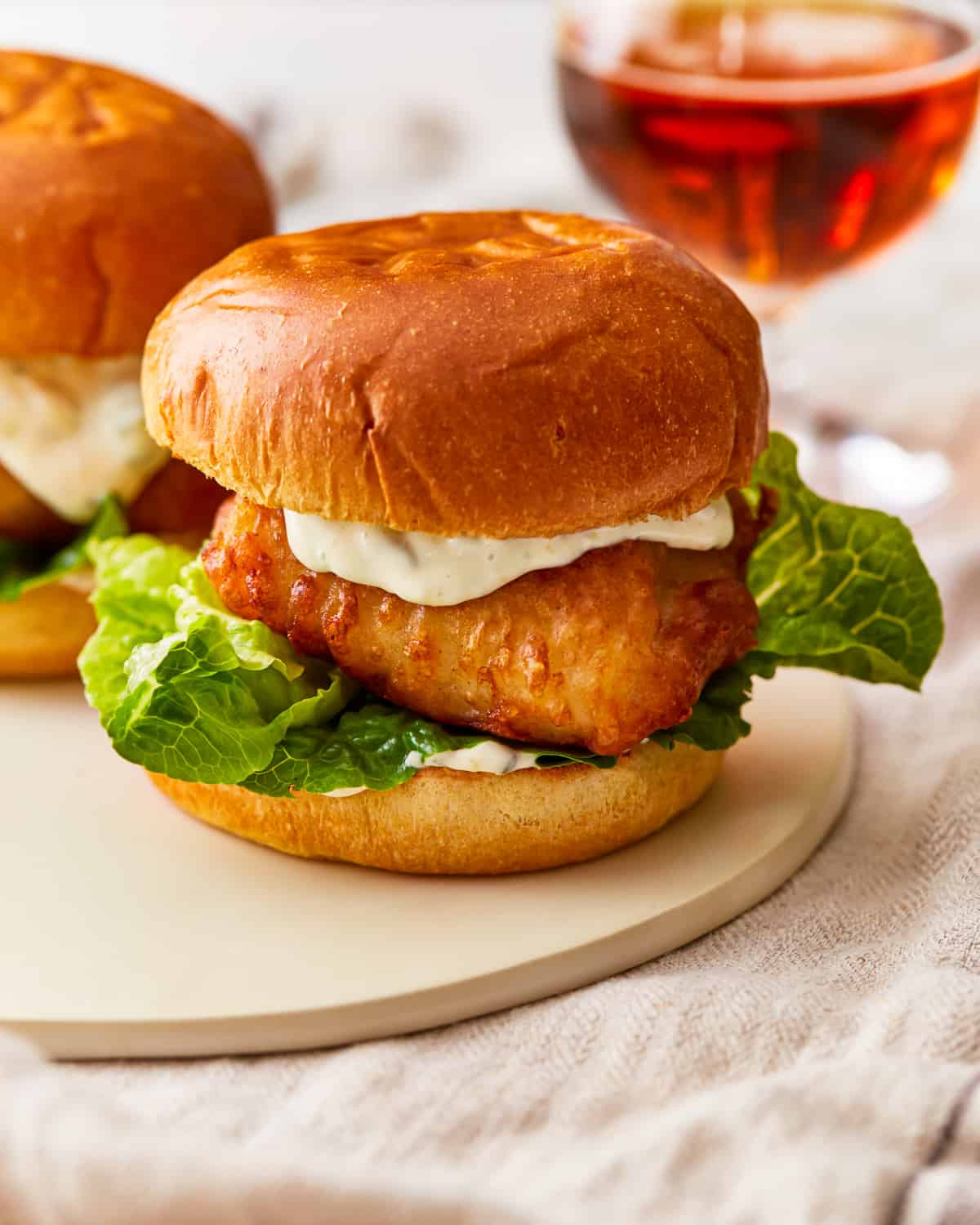 Two fried fish sandwiches on a plate next to a glass of beer.