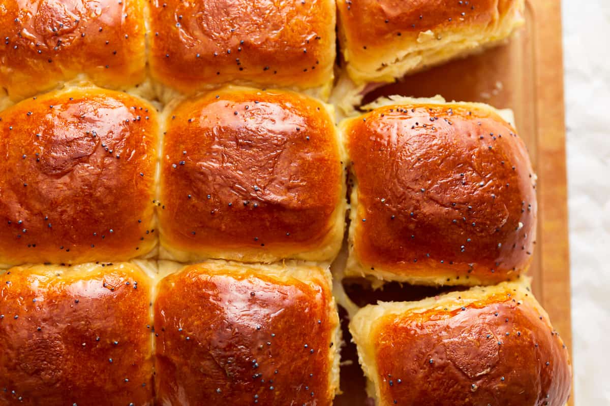 A wooden cutting board with a batch of Hawaiian roll sliders.