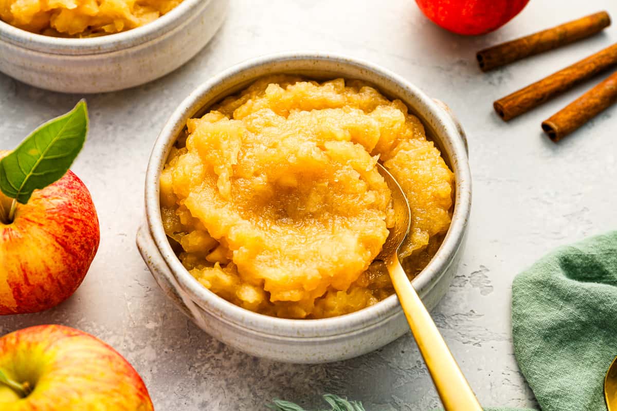 Applesauce in bowls with cinnamon sticks and apples.