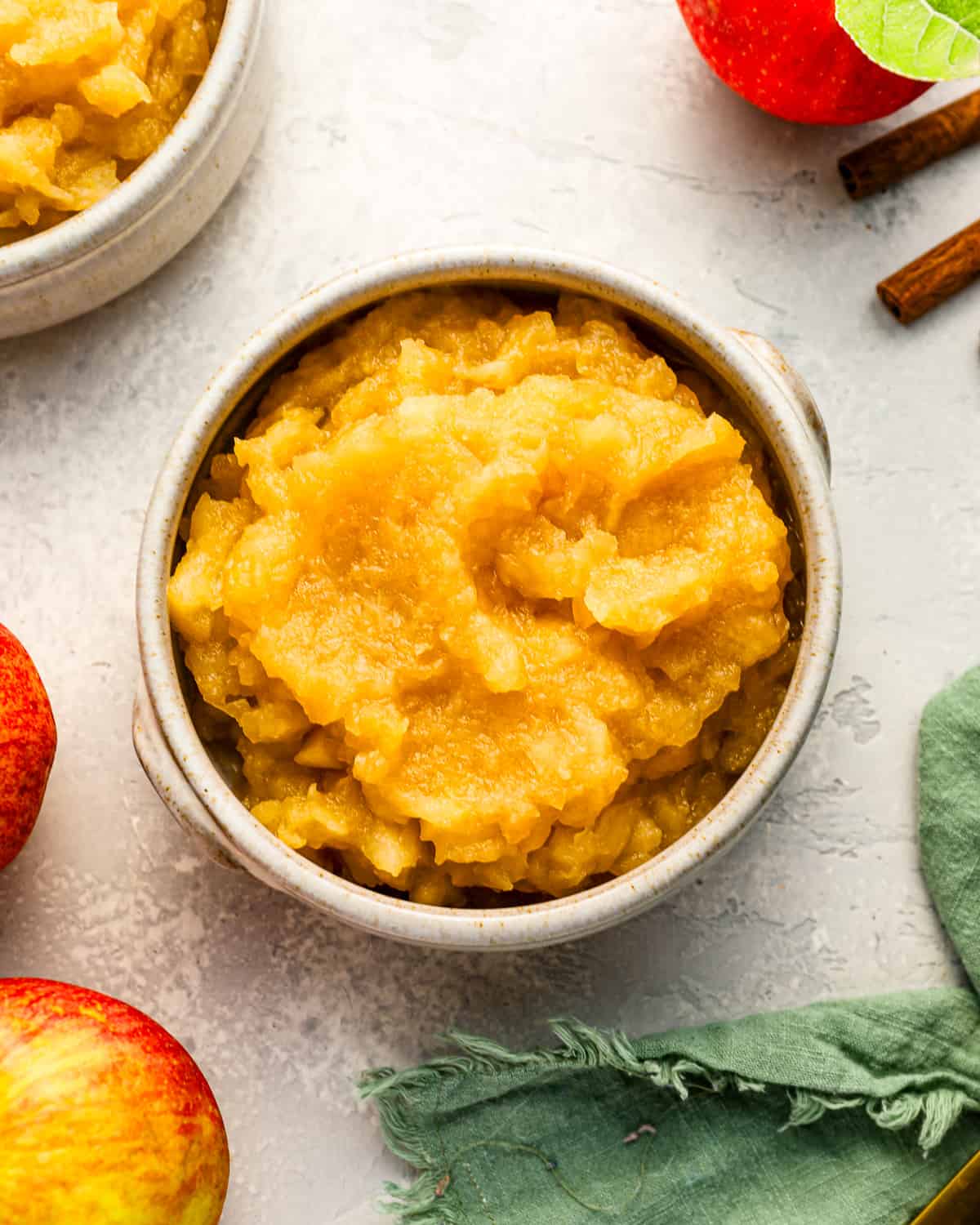 A bowl of homemade applesauce with cinnamon sticks and apples.