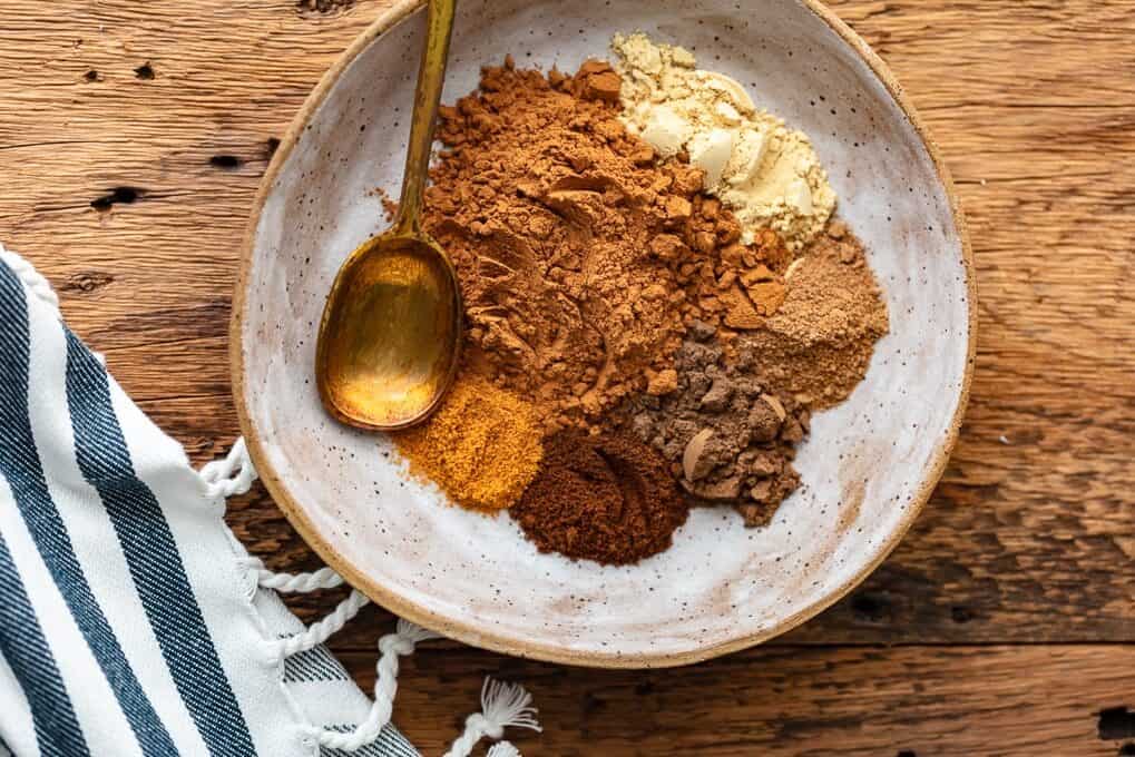 Pumpkin pie spices in a bowl with a spoon on top of a wooden table.