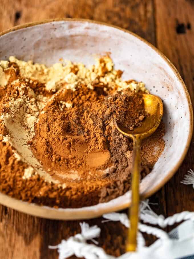 A bowl of pumpkin pie spice with a spoon on a wooden table.