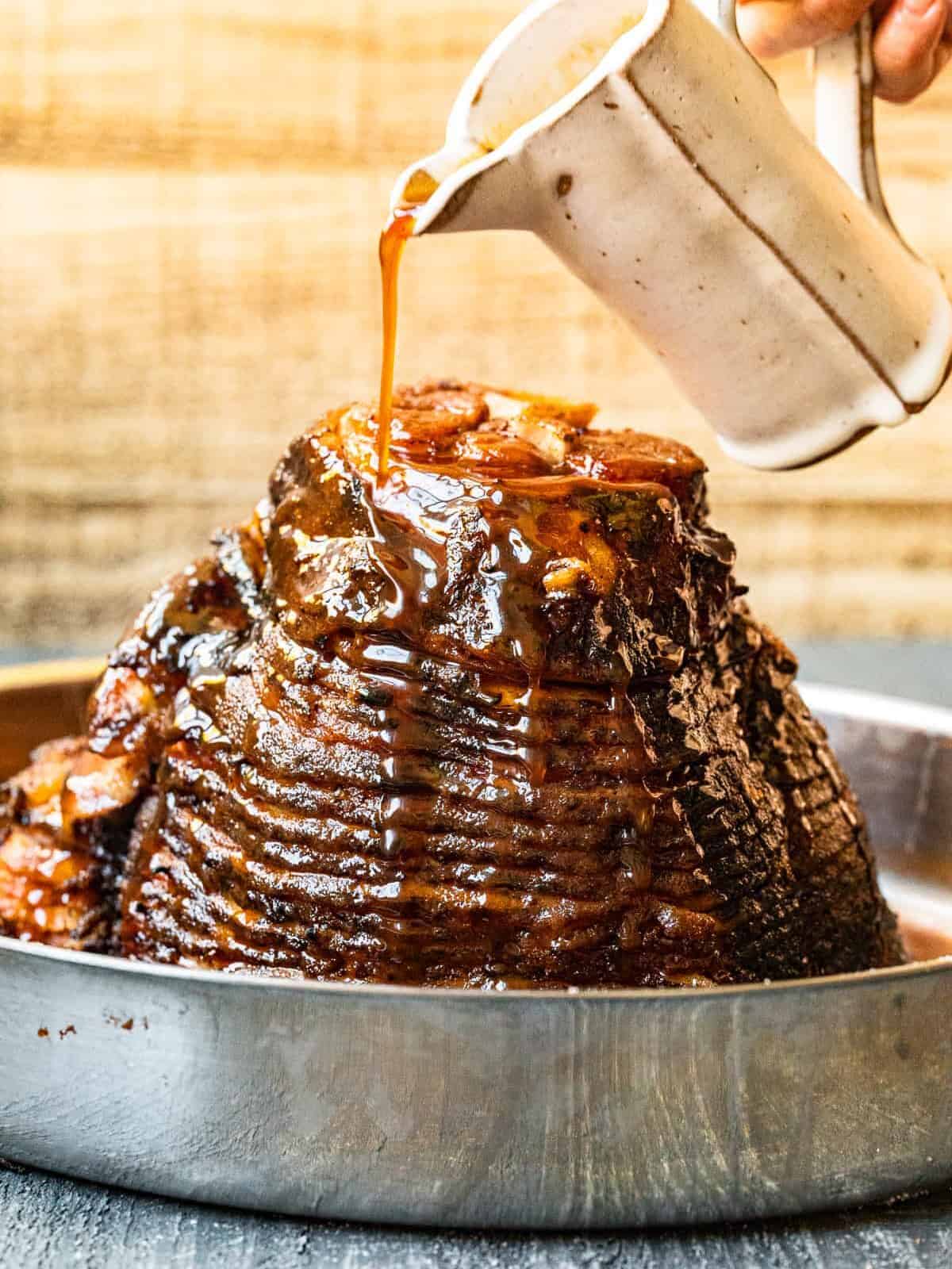 hand pouring glaze onto baked ham