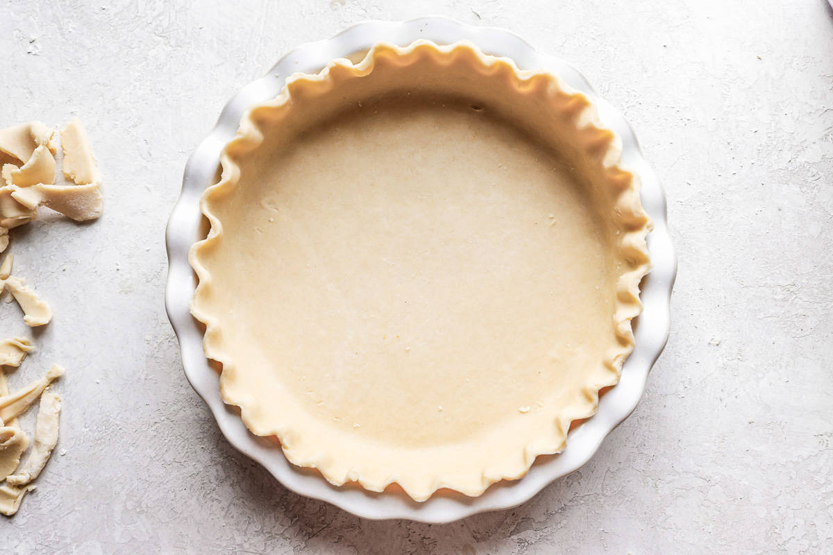 A pie crust in a white dish next to a bowl of pecans.