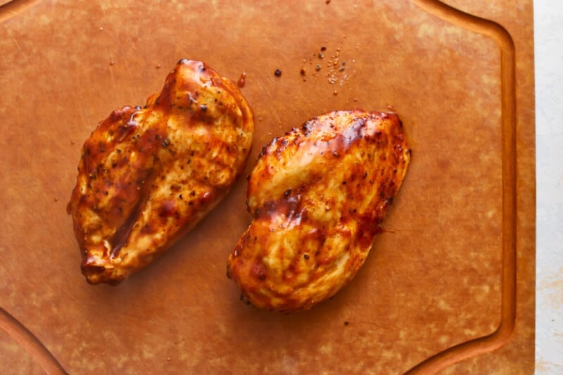Two grilled chicken breasts on a cutting board.