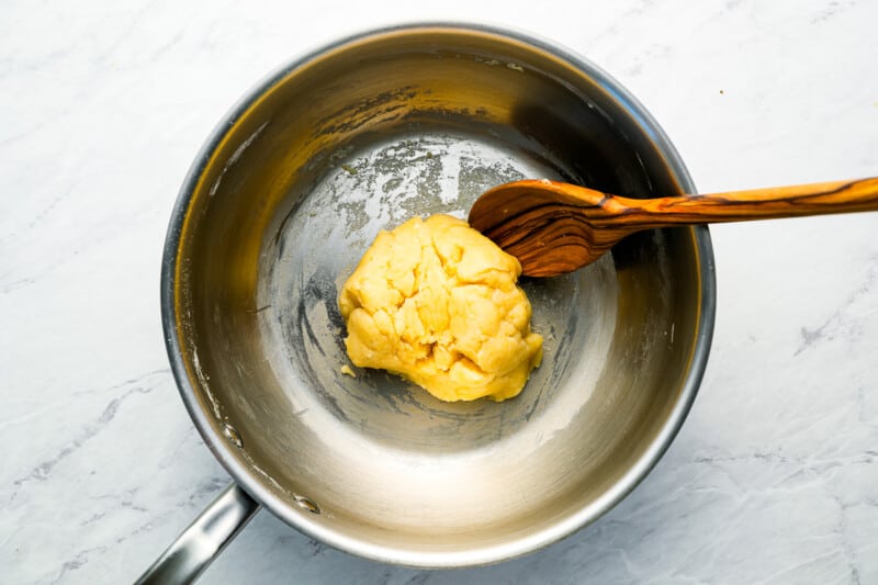 A bowl of dough in a pan with a wooden spoon.