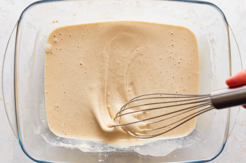 A person whisking a mixture in a glass bowl.