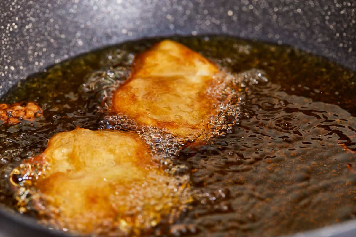 Battered fish fillets frying in a skillet of oil.