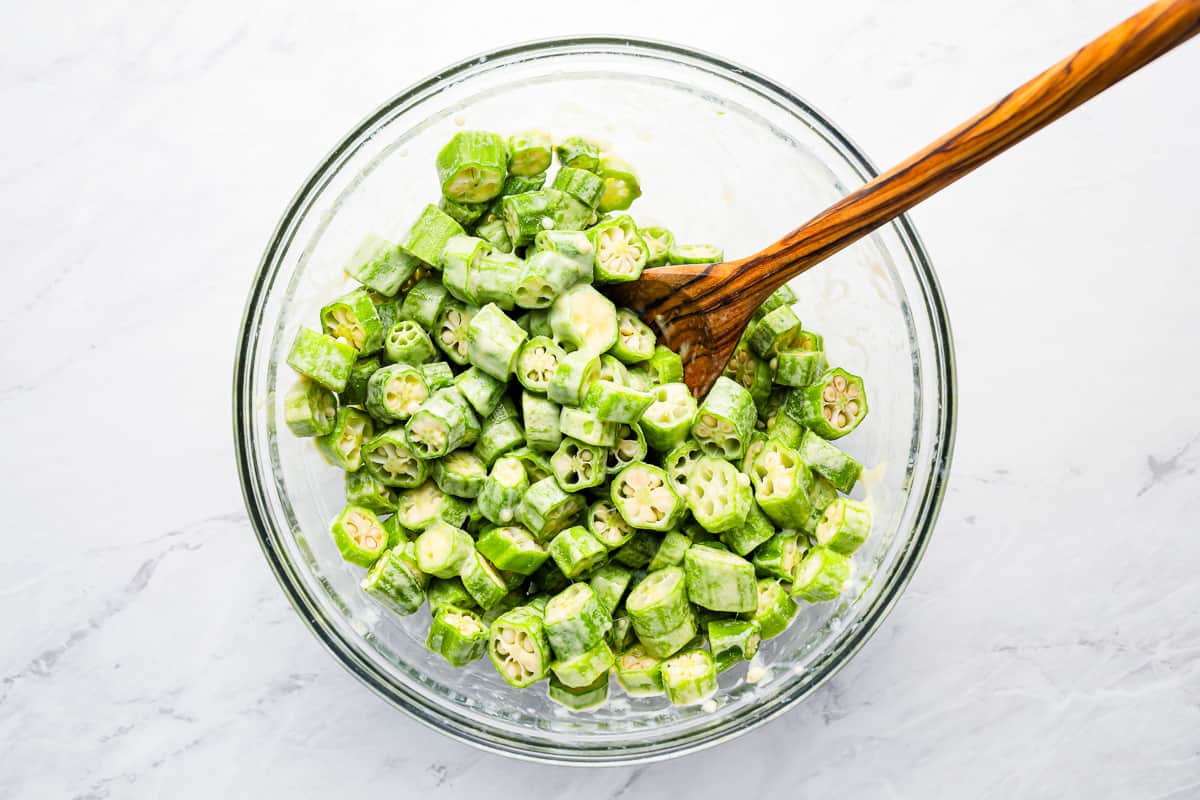 A bowl full of green okra with a wooden spoon.