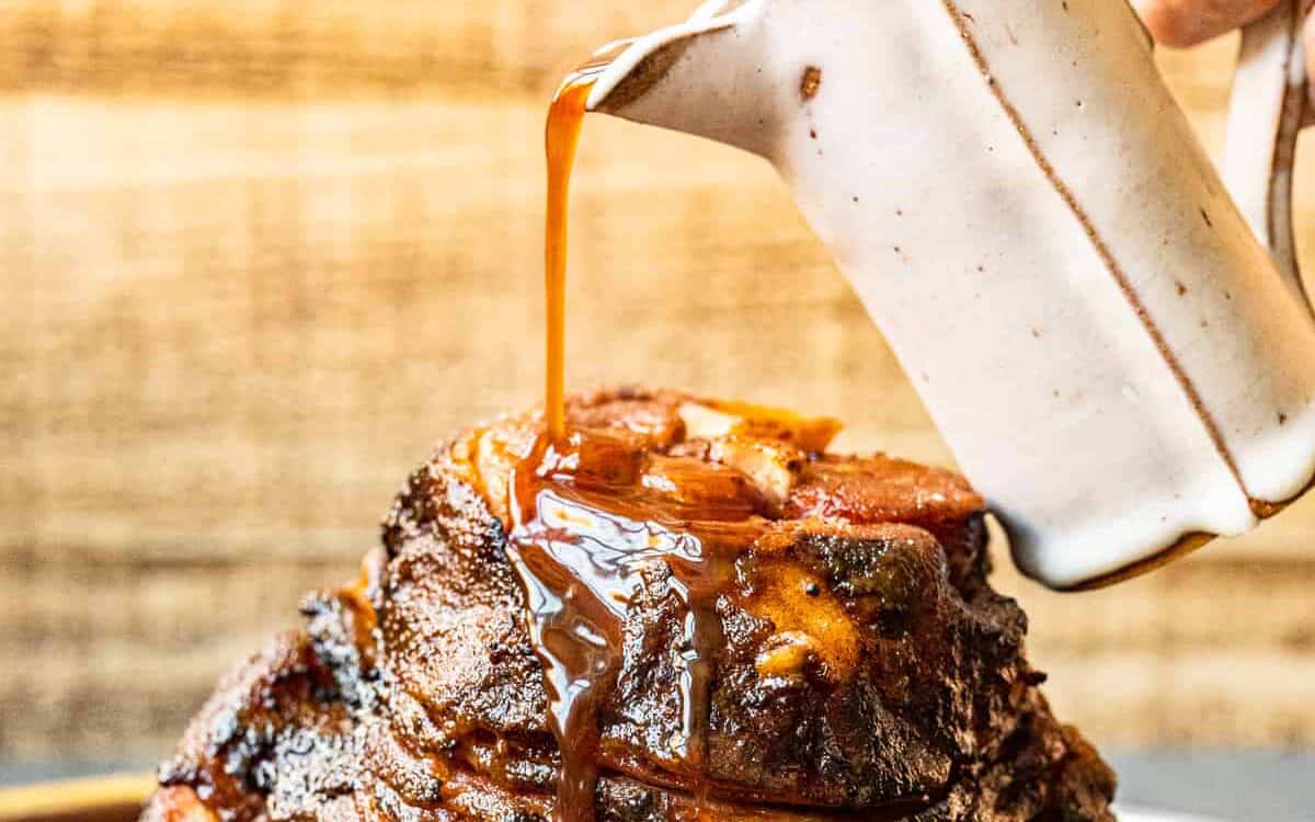 hand pouring glaze onto honey baked ham