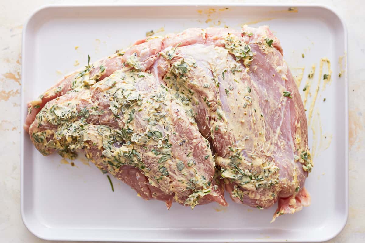 Turkey breast covered with herb butter on a white plate.