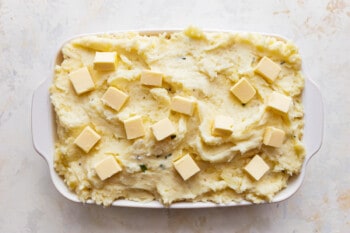 Mashed potatoes with cubes of butter in a white dish.
