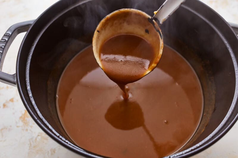 A spoon is being used to stir a sauce in a pot.