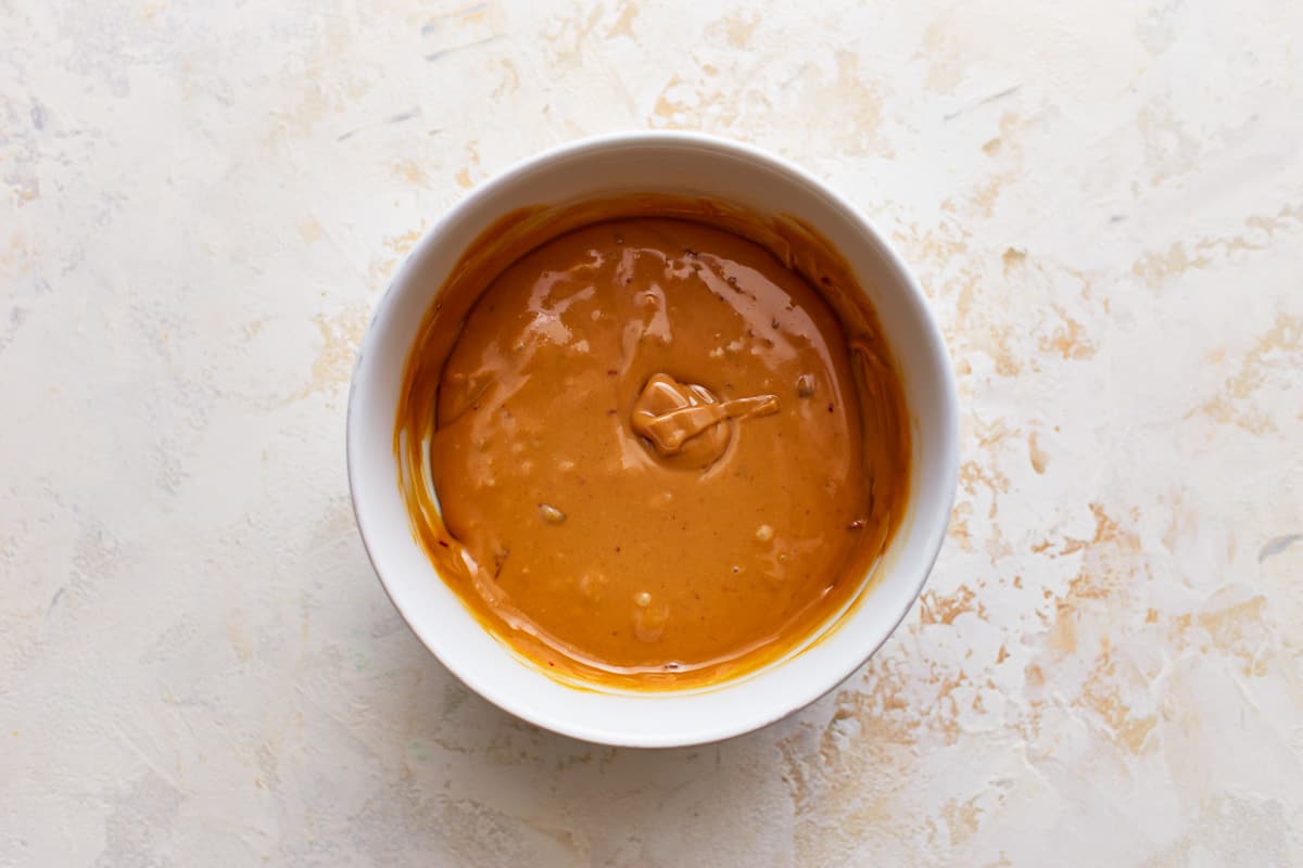 A bowl of peanut butter sauce on a white surface.