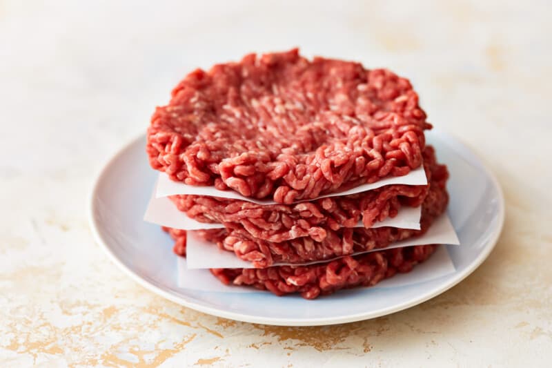 A stack of beef burgers on a plate.