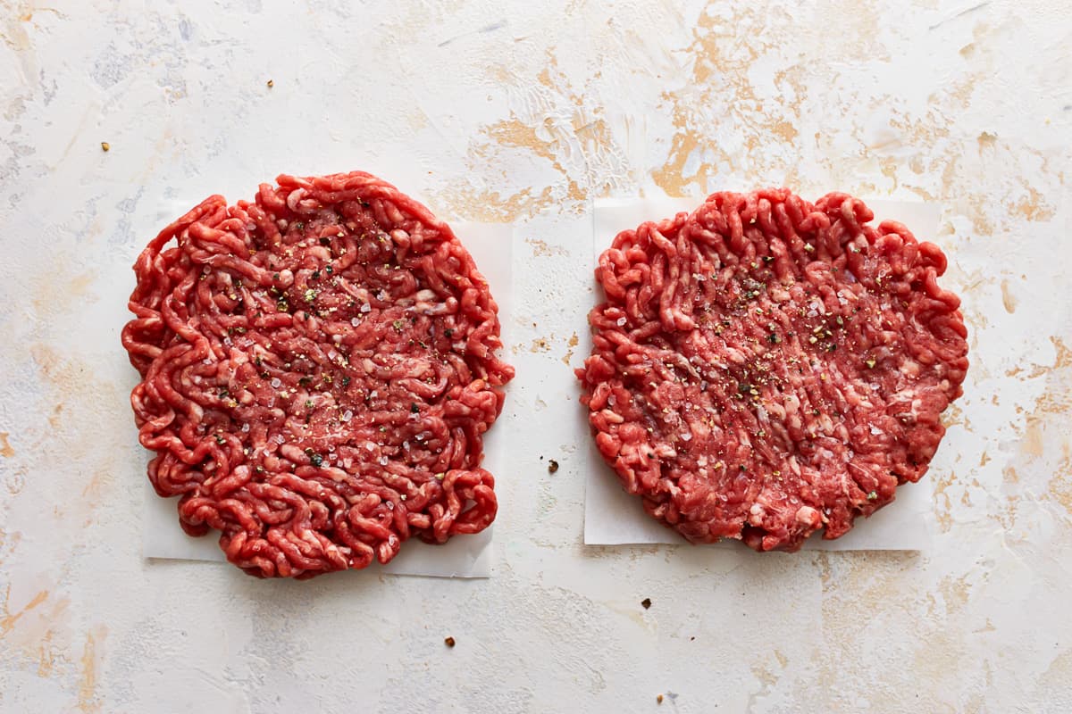 Two raw burger patties on a white surface.