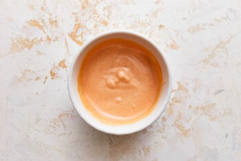 A bowl of burger sauce on a white surface.