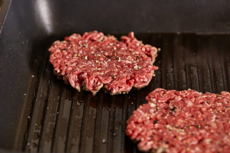 Two beef burgers are being cooked on a grill.