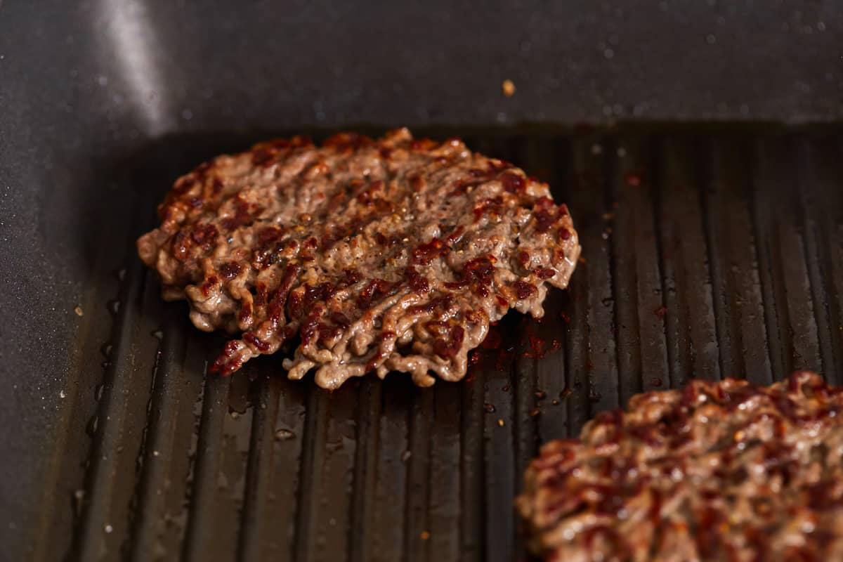 Two hamburger patties are being cooked in a pan.