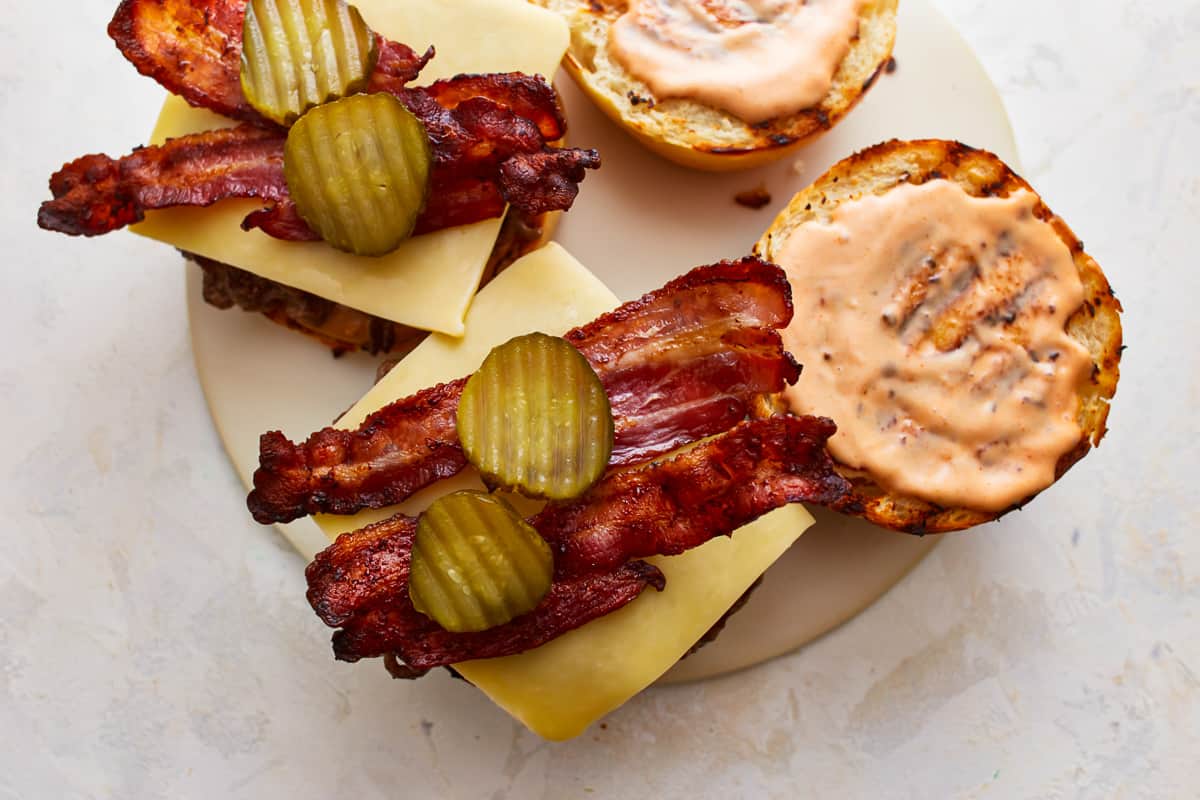 Two burgers topped with slices of bacon and pickles.