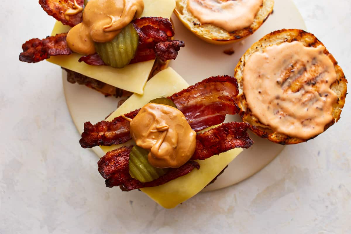 Two burgers topped with bacon, pickles, and dollops of peanut butter.