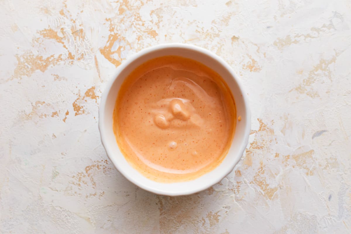 A bowl of burger sauce on a white surface.