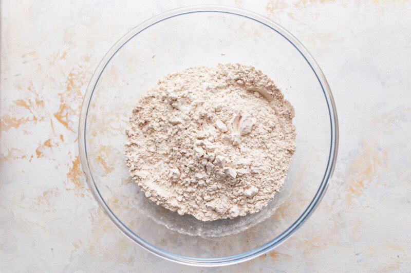 Flour in a glass bowl on a white surface.