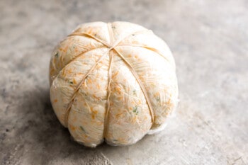 A pumpkin wrapped in plastic on a concrete surface.