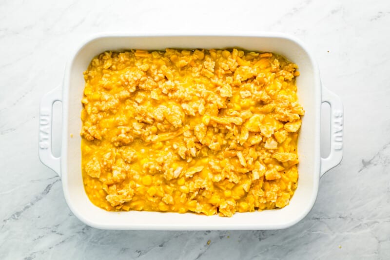 A white baking dish filled with corn casserole topped with ritz crackers.