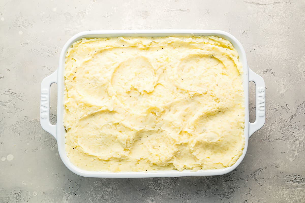 Mashed potatoes in a white dish on a gray surface.