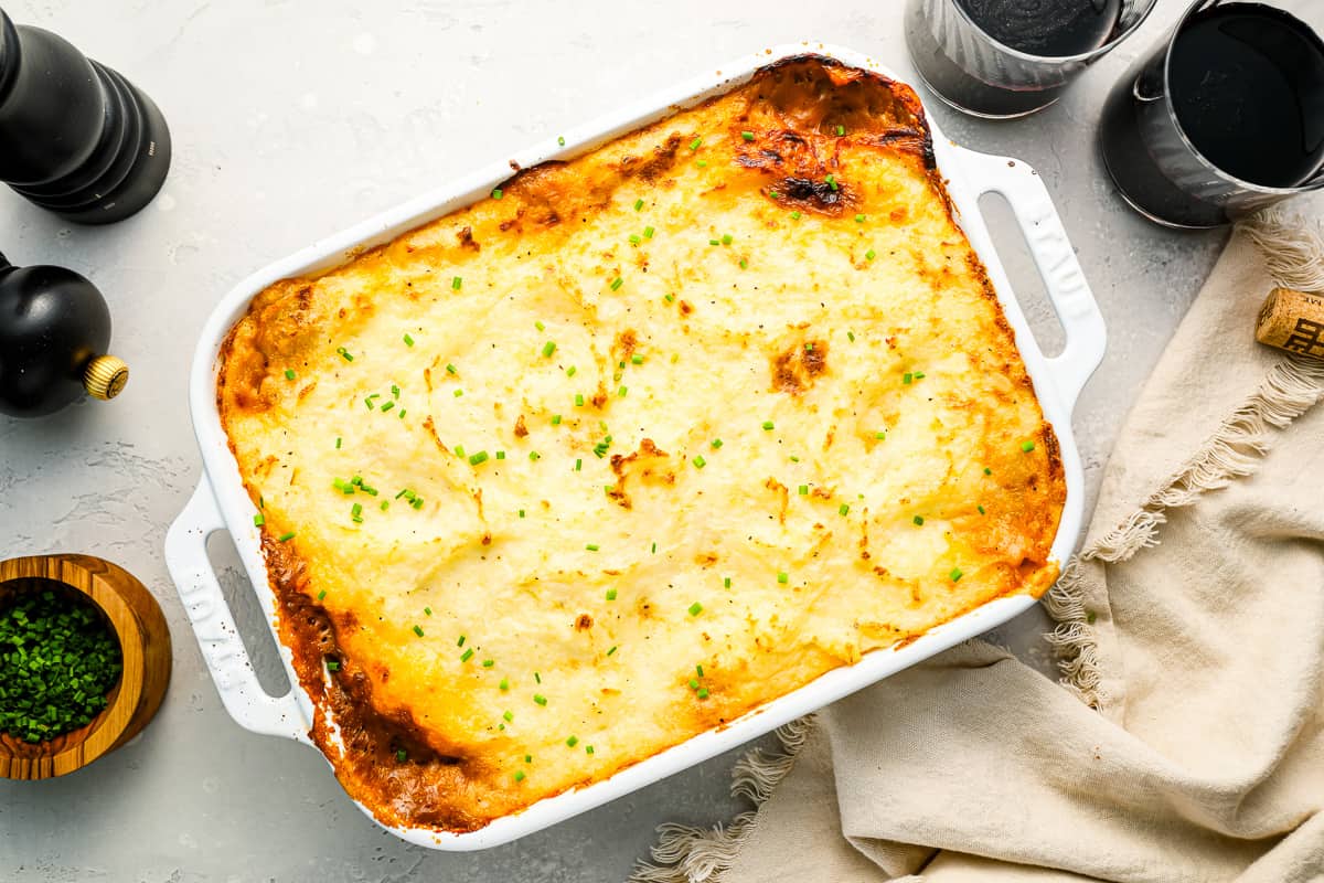 A white dish with a casserole on it next to a bottle of wine.