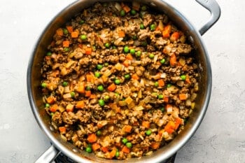 A skillet full of meat, vegetables and peas.