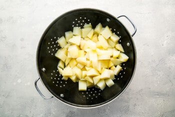 Sliced potatoes in a colander on a gray background.